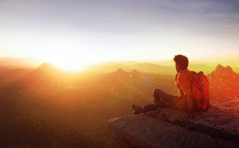 man sitting on edge facing sunset