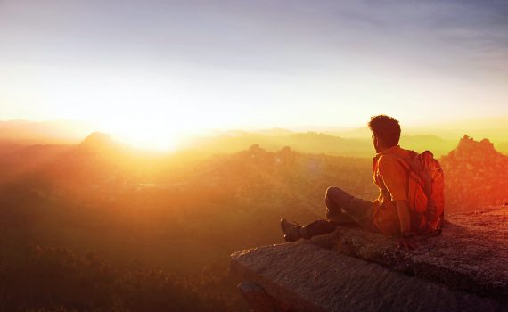 man sitting on edge facing sunset