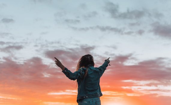 faceless woman pointing with fingers at bright sky in twilight